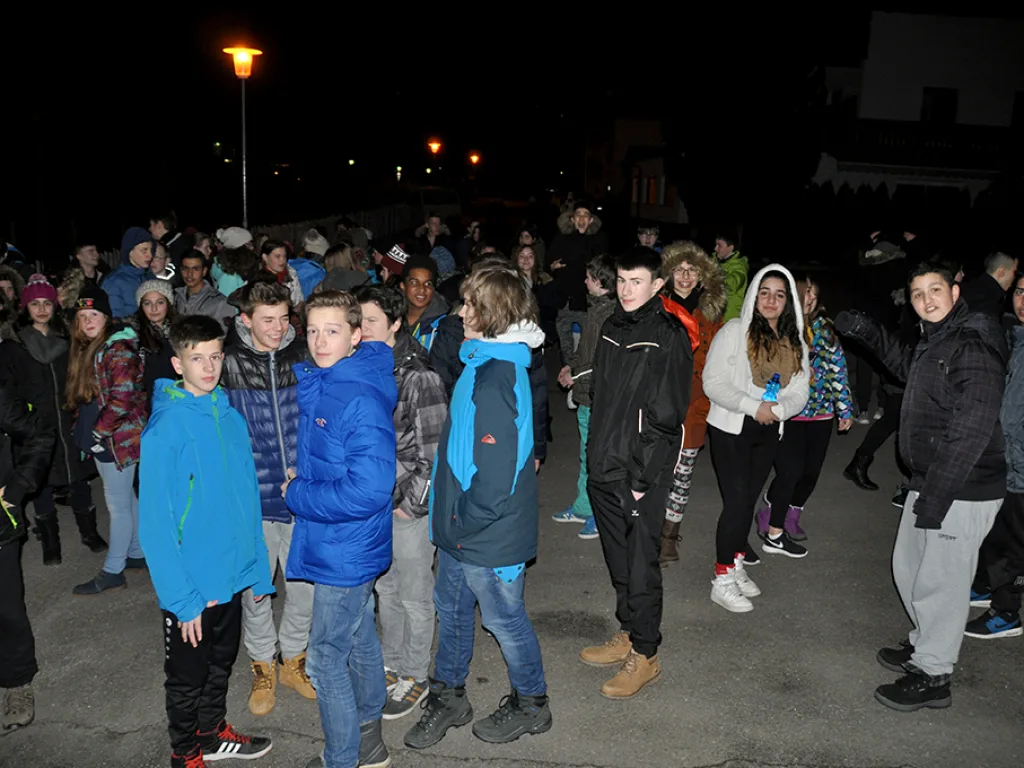 Jugendliche stehen abends in Winterjacken auf einem beleuchteten Platz.